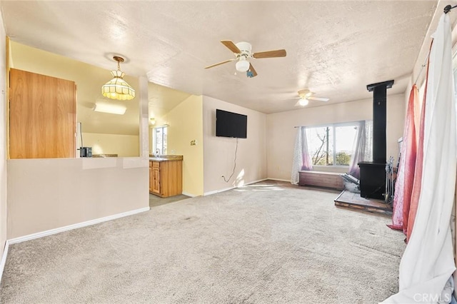 unfurnished living room with ceiling fan, light colored carpet, and a wood stove