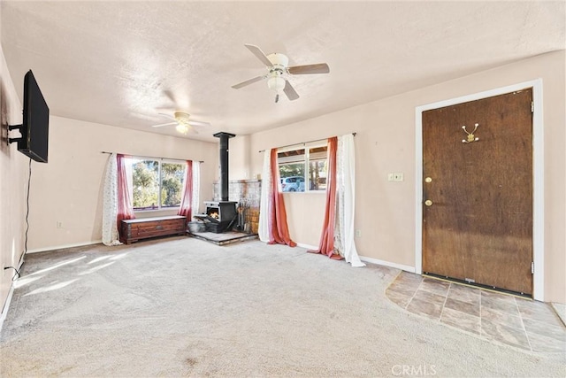 unfurnished living room featuring ceiling fan, carpet flooring, a healthy amount of sunlight, and a wood stove