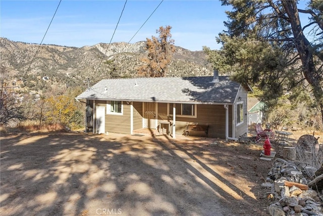 view of front of house with a patio, roof with shingles, and a mountain view