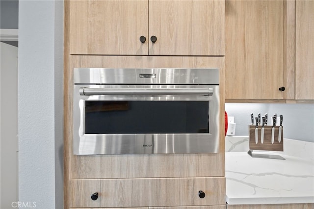 details with stainless steel oven, light brown cabinetry, and light stone countertops