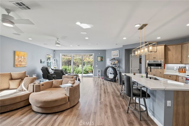 living room with ceiling fan, light hardwood / wood-style floors, and sink