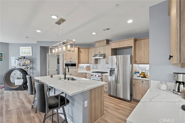 kitchen featuring light stone countertops, appliances with stainless steel finishes, light brown cabinetry, sink, and hanging light fixtures