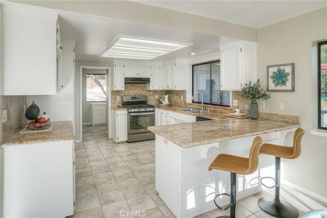 kitchen featuring stainless steel range with gas cooktop, white cabinetry, sink, kitchen peninsula, and light stone countertops