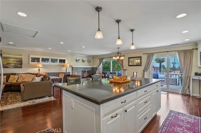 kitchen with dark wood-type flooring, white cabinetry, a center island, a fireplace, and decorative light fixtures