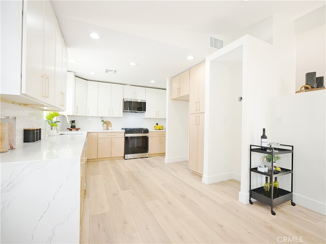 kitchen with light stone countertops, white cabinetry, stainless steel appliances, sink, and light wood-type flooring