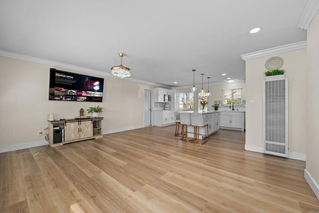 unfurnished living room with sink, crown molding, and light hardwood / wood-style floors