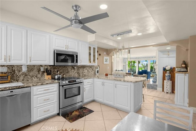 kitchen featuring white cabinets, decorative backsplash, appliances with stainless steel finishes, a peninsula, and light stone countertops