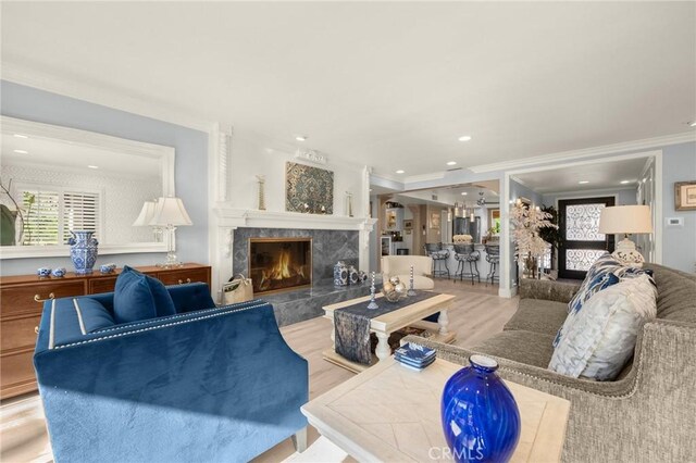 living room with a high end fireplace, light hardwood / wood-style floors, crown molding, and a wealth of natural light