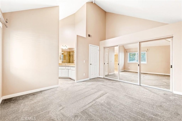 unfurnished bedroom featuring light colored carpet, high vaulted ceiling, and ensuite bath