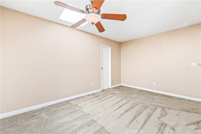 carpeted spare room with ceiling fan, a skylight, and baseboards