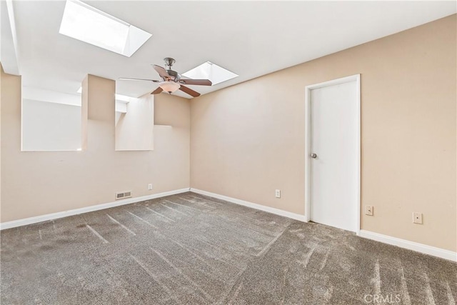 carpeted spare room with a ceiling fan, a skylight, visible vents, and baseboards