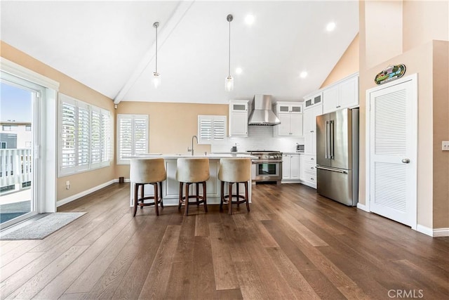 kitchen with high end appliances, glass insert cabinets, wall chimney range hood, white cabinetry, and pendant lighting