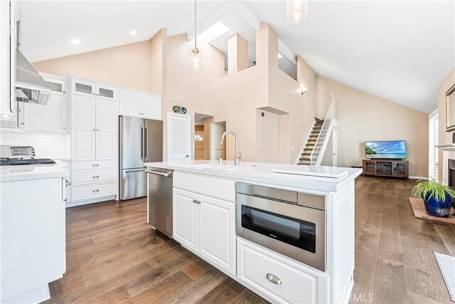 kitchen with a center island with sink, glass insert cabinets, stainless steel appliances, white cabinetry, and a sink