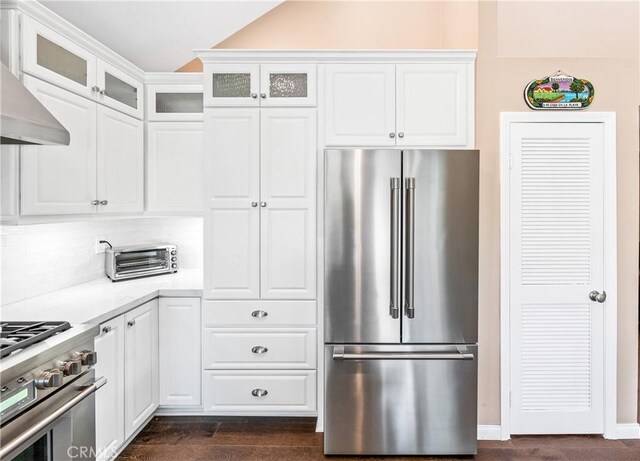 kitchen with white cabinets, light countertops, wall chimney range hood, high end appliances, and glass insert cabinets