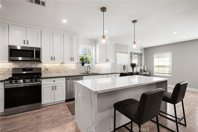 kitchen with appliances with stainless steel finishes, a kitchen island, decorative light fixtures, sink, and light wood-type flooring