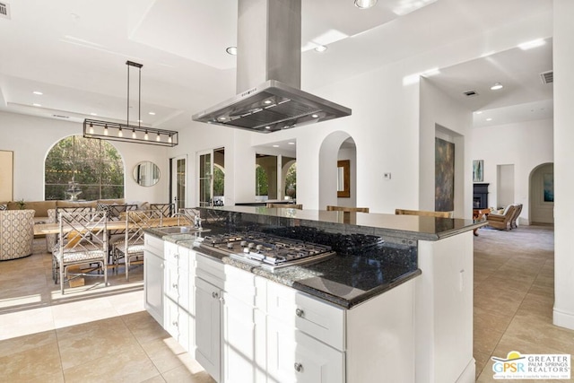 kitchen featuring a spacious island, island exhaust hood, stainless steel gas cooktop, white cabinets, and dark stone counters