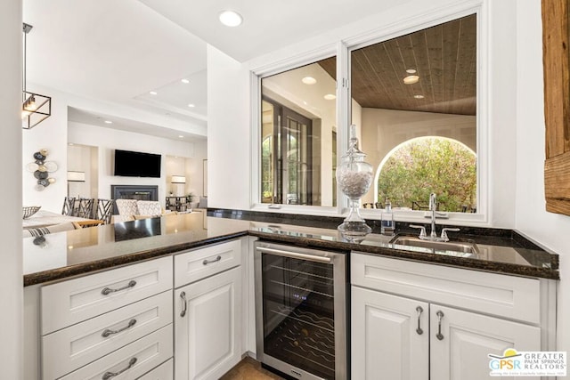 kitchen with white cabinets, dark stone countertops, wine cooler, sink, and hanging light fixtures