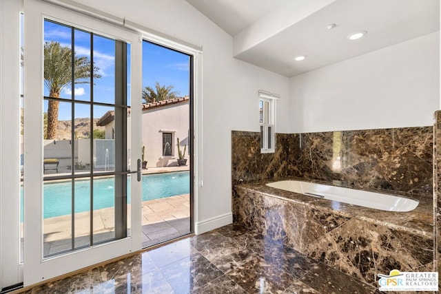 bathroom with tiled bath, a wealth of natural light, and vaulted ceiling