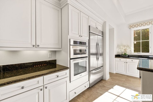 kitchen with light tile patterned floors, appliances with stainless steel finishes, white cabinetry, and dark stone counters