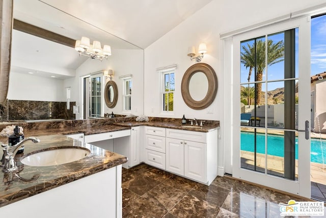 bathroom featuring vaulted ceiling, a chandelier, a healthy amount of sunlight, and vanity