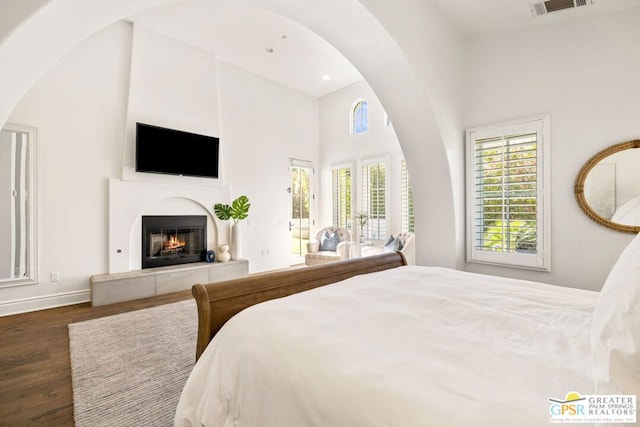 bedroom featuring a towering ceiling, dark wood-type flooring, and a tiled fireplace