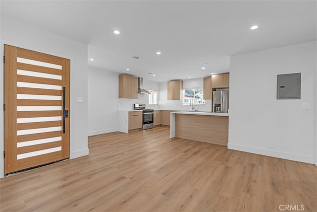 kitchen with light brown cabinets, light hardwood / wood-style flooring, wall chimney exhaust hood, electric panel, and stainless steel appliances