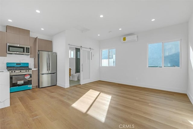 kitchen with a barn door, light hardwood / wood-style flooring, a wall unit AC, and appliances with stainless steel finishes