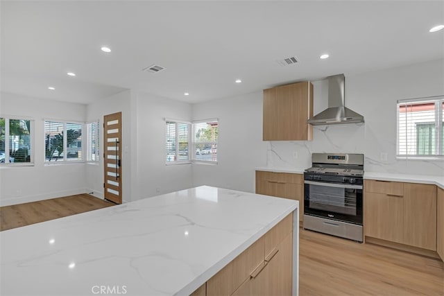 kitchen featuring stainless steel gas stove, wall chimney range hood, a wealth of natural light, and tasteful backsplash