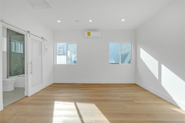 unfurnished room featuring a wall mounted AC, a barn door, and light wood-type flooring