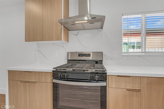 kitchen with wall chimney exhaust hood, gas stove, light brown cabinets, backsplash, and light stone counters