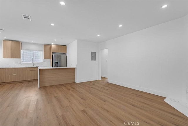 kitchen featuring electric panel, sink, stainless steel fridge, and light wood-type flooring