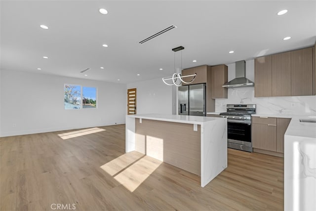 kitchen featuring light wood-type flooring, a kitchen island, decorative light fixtures, stainless steel appliances, and wall chimney exhaust hood