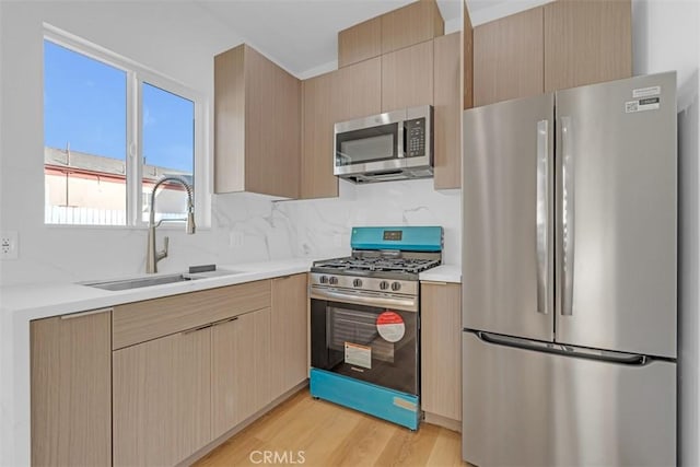 kitchen featuring appliances with stainless steel finishes, sink, light wood-type flooring, backsplash, and light brown cabinets