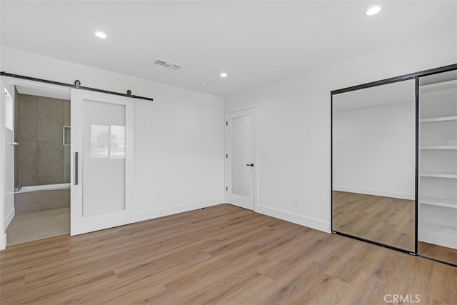 unfurnished bedroom with a closet, a barn door, and light wood-type flooring