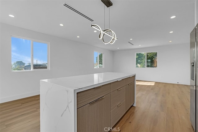 kitchen with light wood-type flooring, a kitchen island, light stone countertops, and decorative light fixtures