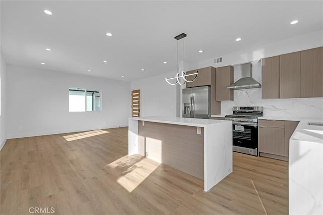 kitchen with decorative light fixtures, tasteful backsplash, a center island, wall chimney range hood, and stainless steel appliances