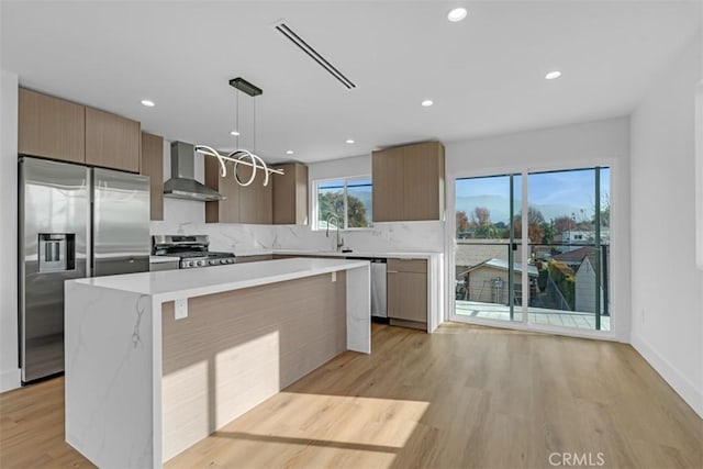 kitchen featuring a kitchen island, decorative light fixtures, light hardwood / wood-style flooring, stainless steel appliances, and wall chimney exhaust hood