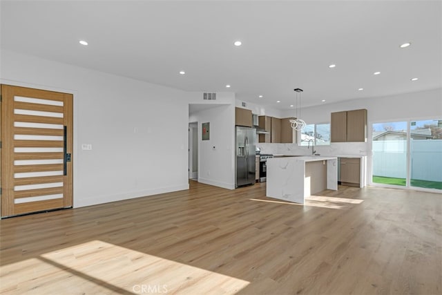 kitchen with appliances with stainless steel finishes, decorative light fixtures, tasteful backsplash, a kitchen island, and light hardwood / wood-style floors