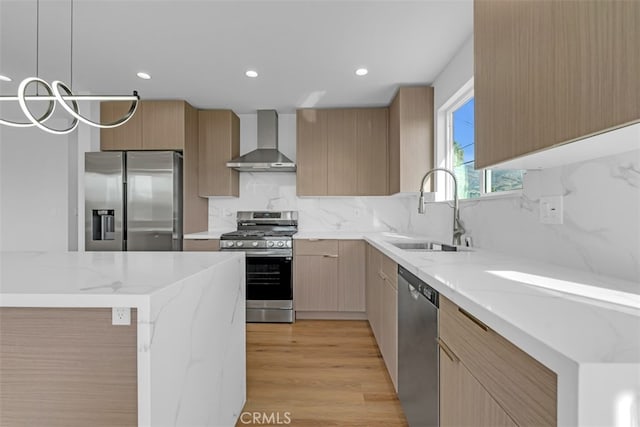 kitchen with pendant lighting, wall chimney exhaust hood, sink, backsplash, and stainless steel appliances