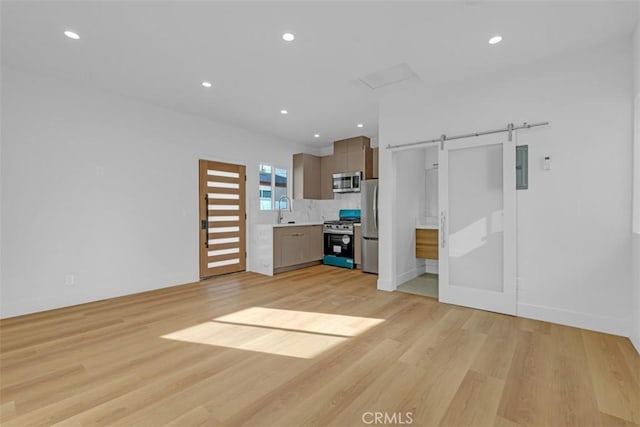 unfurnished living room with sink, light hardwood / wood-style floors, and a barn door