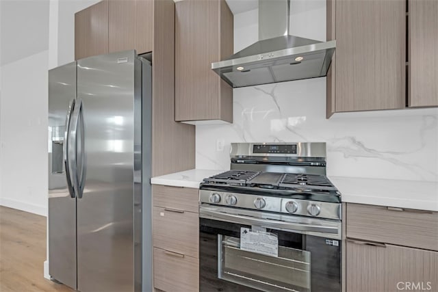 kitchen featuring light stone countertops, light wood-type flooring, backsplash, stainless steel appliances, and wall chimney exhaust hood