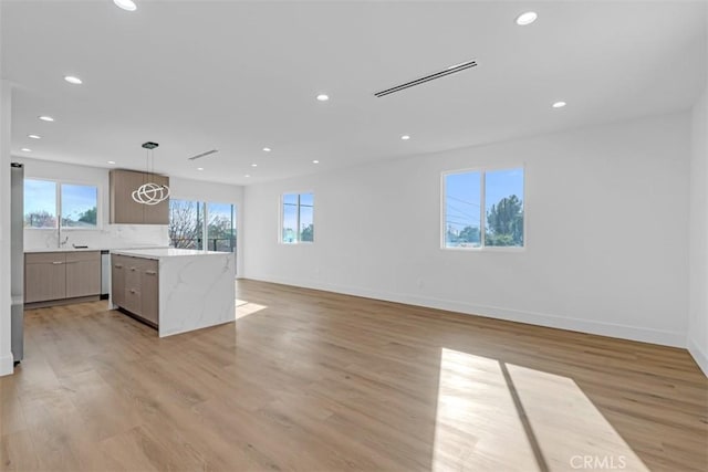 kitchen with hanging light fixtures, light hardwood / wood-style floors, a spacious island, and light stone counters