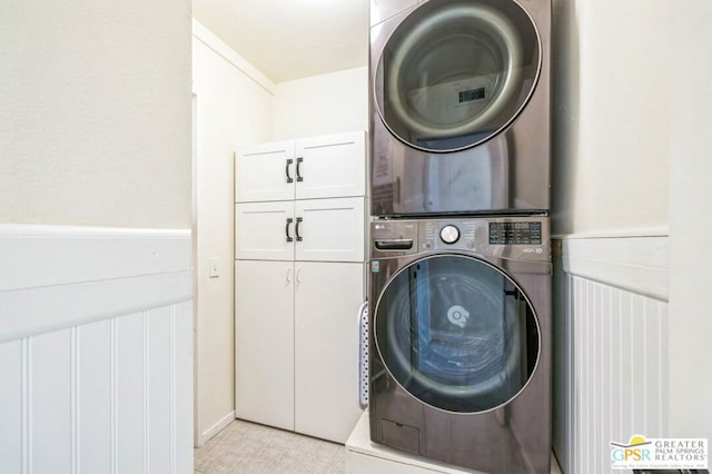 laundry room featuring stacked washer / dryer, light tile patterned floors, and cabinets