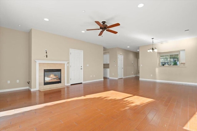 unfurnished living room featuring ceiling fan with notable chandelier, wood-type flooring, and a tile fireplace