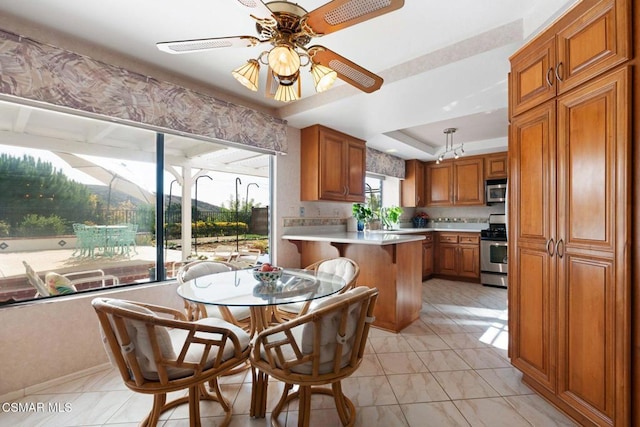 kitchen featuring a kitchen breakfast bar, ceiling fan, appliances with stainless steel finishes, and a raised ceiling