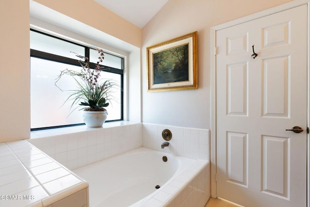 bathroom featuring a relaxing tiled tub and vaulted ceiling