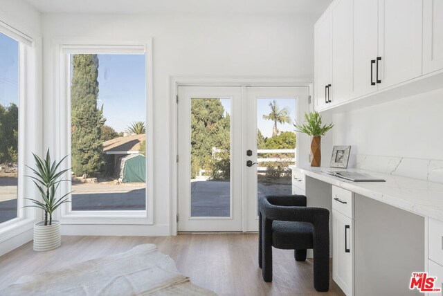 doorway to outside with light hardwood / wood-style flooring, built in desk, a healthy amount of sunlight, and french doors