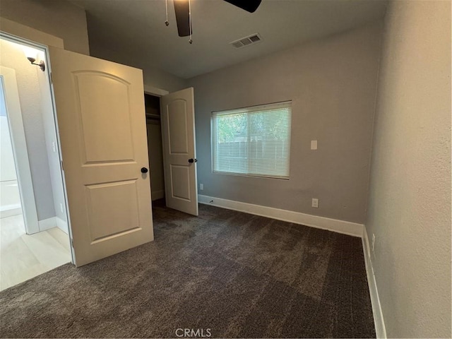 unfurnished bedroom with ceiling fan and dark carpet