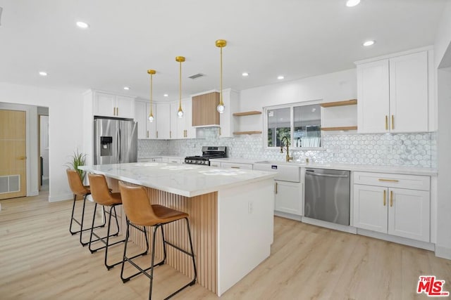 kitchen featuring white cabinets, a kitchen island, stainless steel appliances, sink, and hanging light fixtures