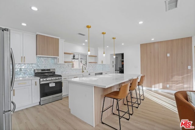 kitchen with white cabinets, a center island, stainless steel appliances, hanging light fixtures, and light stone counters